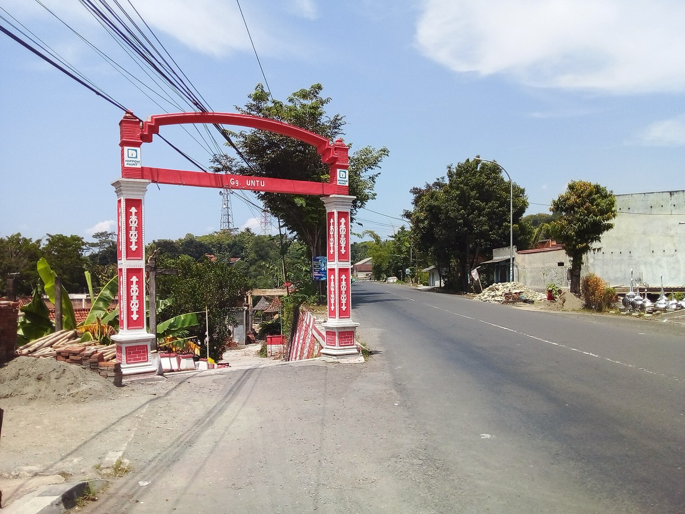 Gapura merah di mulut gang kampung, jalan aspal di sebelahnya
