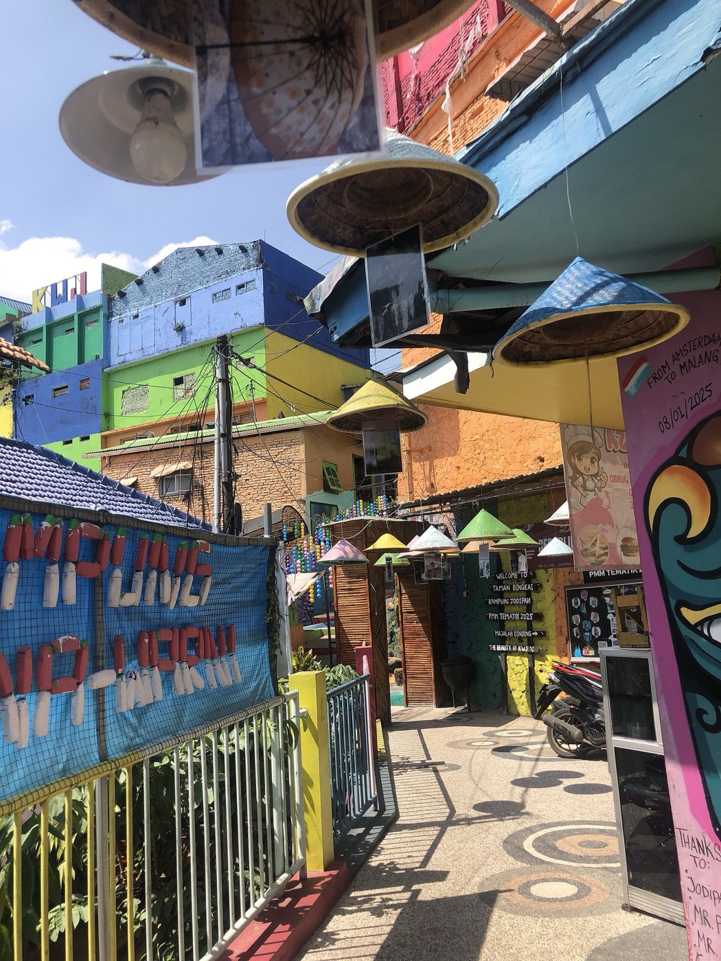 Lorong kampung berwarna-warni dengan caping dan mural