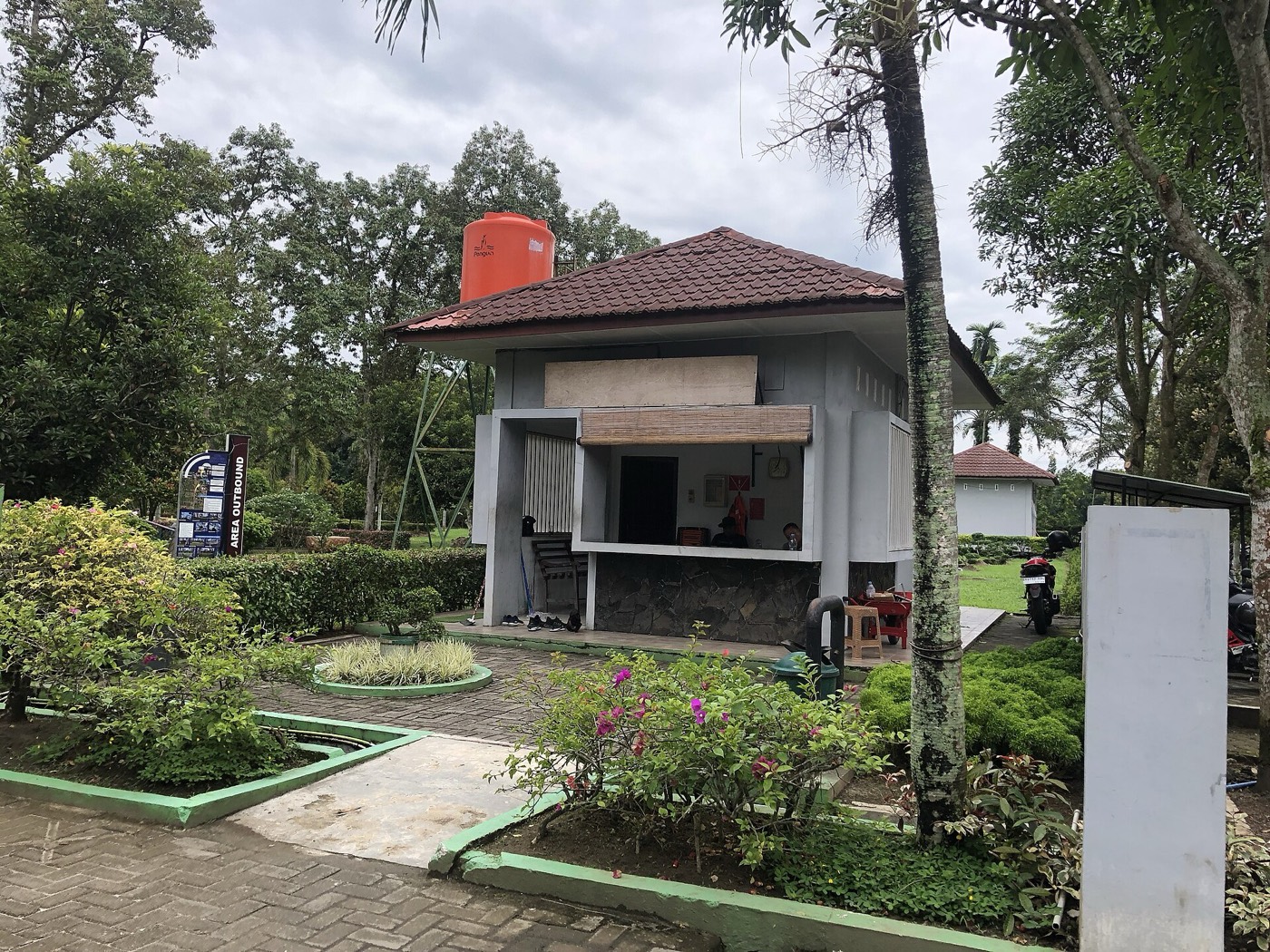 Pos satpam di pintu masuk taman perumahan, dikelilingi pepohonan